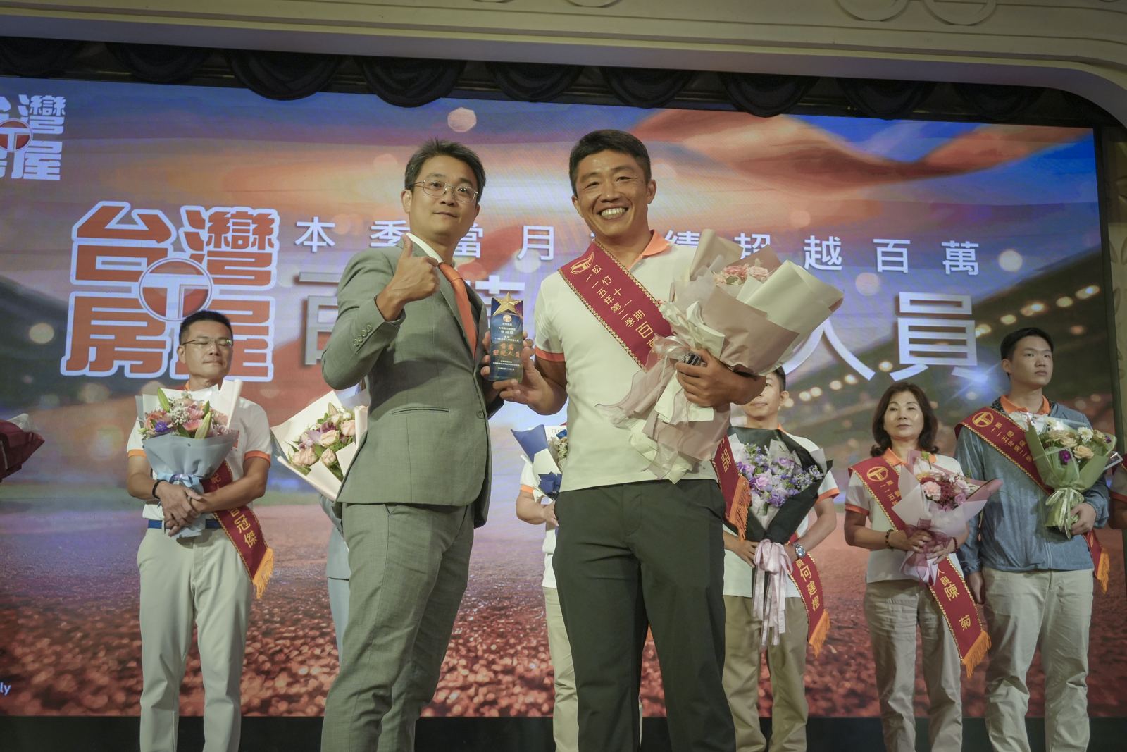 三瀛夥伴在台灣房屋頒獎台上領獎，手持獎盃與花束